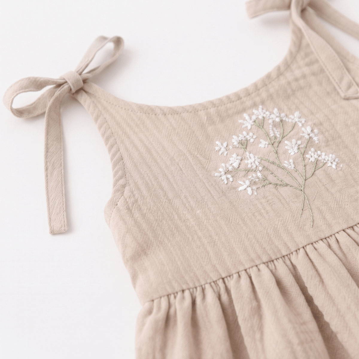 Claire Muslin Baby Girl Dress in Claire Beige with delicate floral embroidery and tie straps.