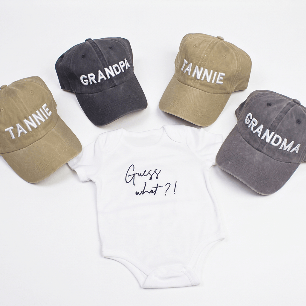 Guess What New Parents Announcement Cap Gift Box featuring caps for grandparents and a onesie with Guess what?! design.