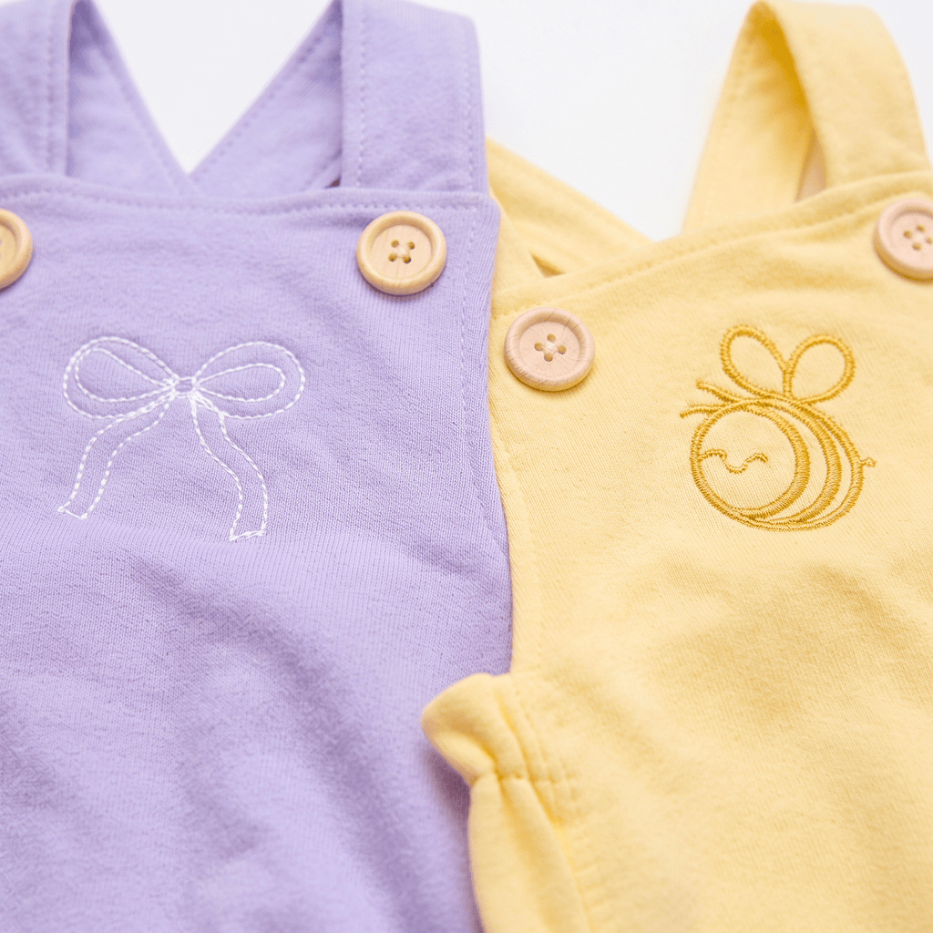 Embroidered Cotton Baby Romper featuring a white bow and a golden bee on lavender and yellow backgrounds.