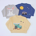 Three children's ribbed knit sweaters laid flat on a white background: a light gray sweater with a white bunny motif, a royal blue sweater with a yellow sun and car motif, and a pale yellow sweater with a teal truck motif.